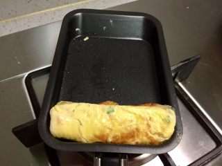 5、香葱火腿厚蛋烧,把第一层蛋皮卷起。