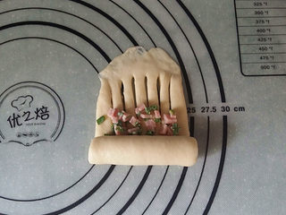 11、香葱火腿面包卷,在划口的下端地方，放少许香葱火腿碎（要预留些、后面还有用），再自下向上卷起