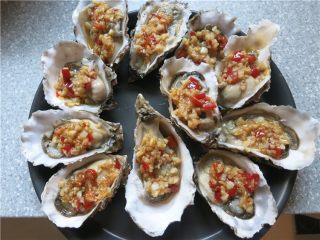11、蒜蓉生蚝烤烤更美味,将炒好的蒜蓉用勺舀到生蚝上,放入披萨盘中