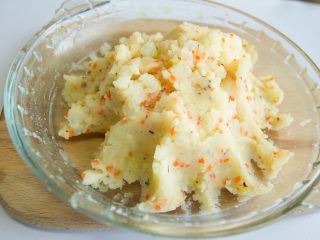 4、香酥烤蘑菇,把准备好的罗勒叶、大蒜沫、柠檬皮，胡萝卜碎放入土豆泥的碗中，挤入少许柠檬汁，撒上盐和黑胡椒粉，放上芝士碎，搅拌均匀。