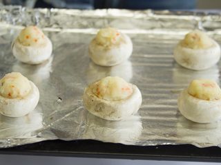 5、香酥烤蘑菇,用小勺把土豆泥塞到蘑菇里，不用塞很紧，但是尽量多堆一些，还可以在上面裹上一些芝士碎，放到铺有锡纸的烤盘上（可以先在要放蘑菇的位置刷 一点点油