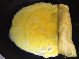 15、虾仁鸡蛋卷,卷到剩1/3蛋皮的时候，在左侧倒入剩余的蛋液，同样转动平底锅，让蛋液和之前剩余的蛋皮完全融合