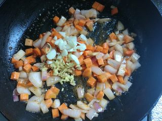 5、剩米饭华丽大变身——虾仁焗饭,接着放入红萝卜丁，翻炒两下，放入蒜片姜末翻炒均匀。