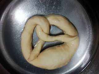 13、德式碱水包,用100克的温水（大概30-40度），溶解4克烘焙碱，把冷冻好的面团在水里浸泡30秒，然后捞出放在铺有有多层油纸的烤盘里面。