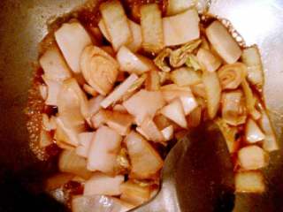 3、韩国辣炒年糕片家庭版,将切好的年糕和洋葱倒入翻炒，顺势加少许盐，加入少许开水，盖锅中火煮约10分钟