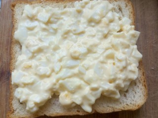 3、鸡蛋三明治,先拿一片把夹心铺上。