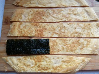 6、年夜菜~锦绣苔味香肠卷,摊好的鸡蛋饼取出光面朝下，用刀分切成与海苔同宽的条状