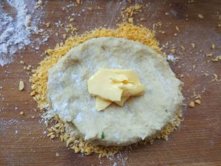 6、奶酪流心豆浆可乐饼,将少许面包糠倒在操作板上，挖一勺土豆肉泥，蘸少许干面粉压平，撕少许切达奶酪，再将肉饼包好封口，翻面蘸满面包糠