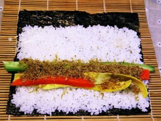 6、家庭寿司,铺好海苔,毛面朝上,铺满米饭,最尾端留点位置,否则一会卷的时候米饭会冒出来。放入黄瓜、胡萝卜、蛋皮、肉松卷起来,卷紧。