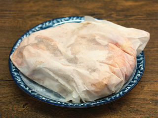 3、珐琅锅盐焗鸡,将半只鸡包裹起来，用细小的针头在油纸上戳些小孔，粗盐加热时，会形成一股水蒸气，便于盐粉的香气渗透到鸡肉中，包裹好的鸡肉放在一旁待用