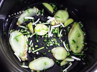 2、盐焗手撕鸡,在冰箱里腌制半天以上。鸡腌制好了,在电饭煲里倒两勺油,晃匀。姜切薄片,葱切段,和腌制用的葱姜一起,均匀在电饭锅底,铺满。
